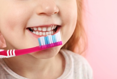 Little girl brushing teeth on color background, closeup