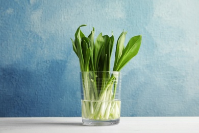 Glass of wild garlic or ramson on table against color background