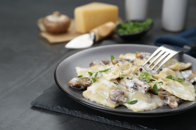 Photo of Delicious ravioli with tasty sauce and mushrooms served on black table, closeup