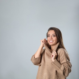 Photo of Young woman in stylish brown sweater on grey background, space for text