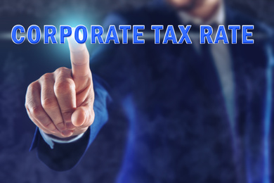 Image of Corporate tax rate. Man touching virtual screen on color background, closeup