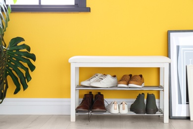 Photo of Collection of stylish shoes on rack storage near color wall in room