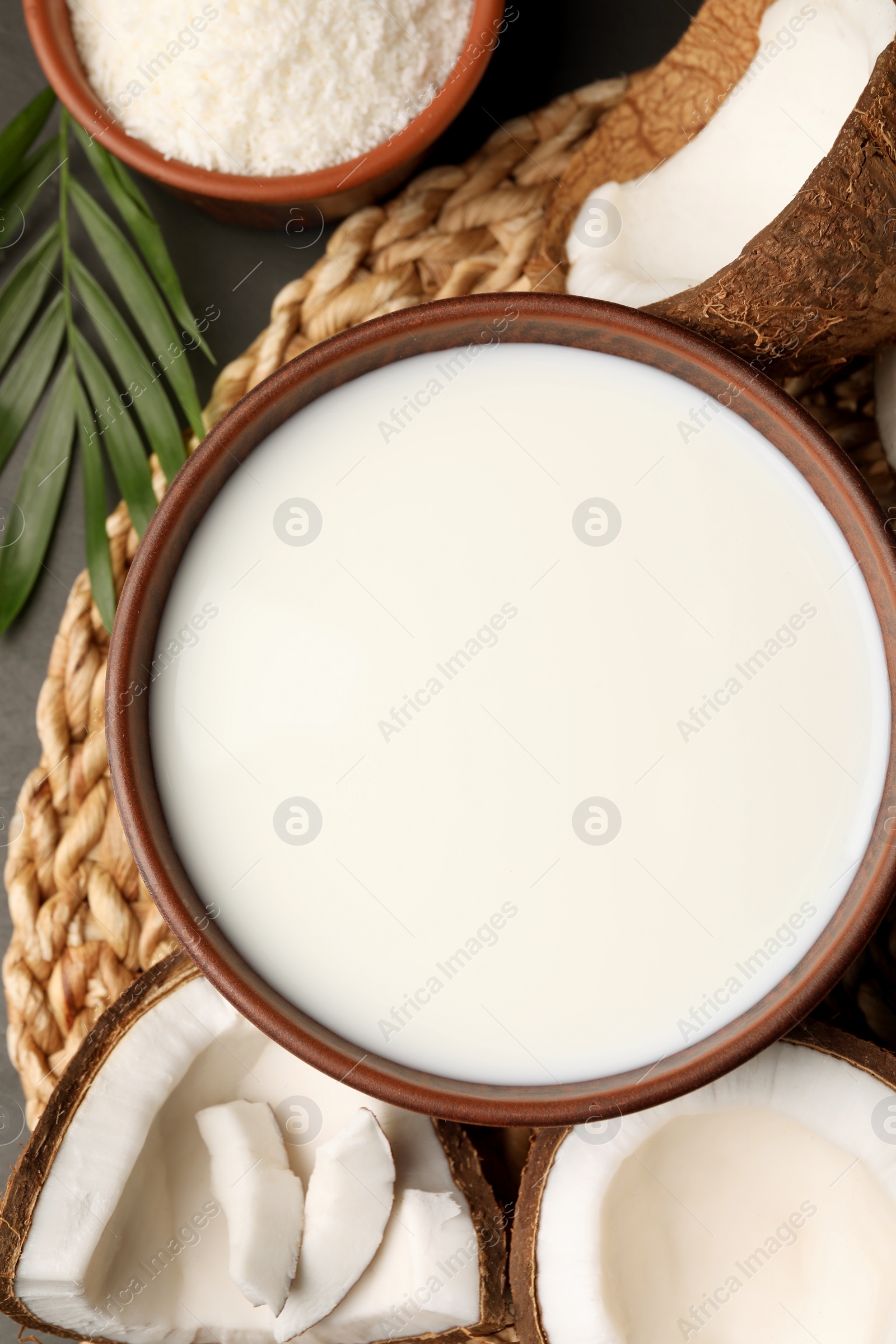 Photo of Bowl of delicious vegan milk near coconut pieces on grey table, flat lay