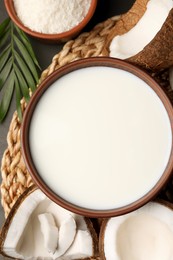 Photo of Bowl of delicious vegan milk near coconut pieces on grey table, flat lay