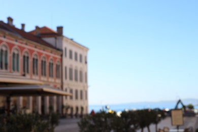 Photo of Blurred view of buildings with arched windows and square near sea under blue sky