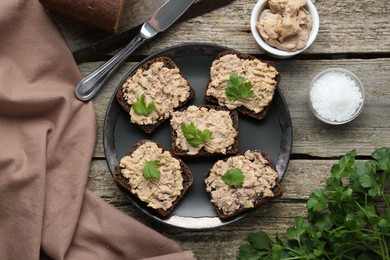 Photo of Tasty sandwiches with cod liver, salt and parsley on wooden table, flat lay