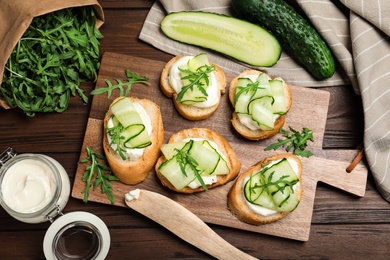 Photo of Flat lay composition of tasty bruschettas with cucumbers on wooden table