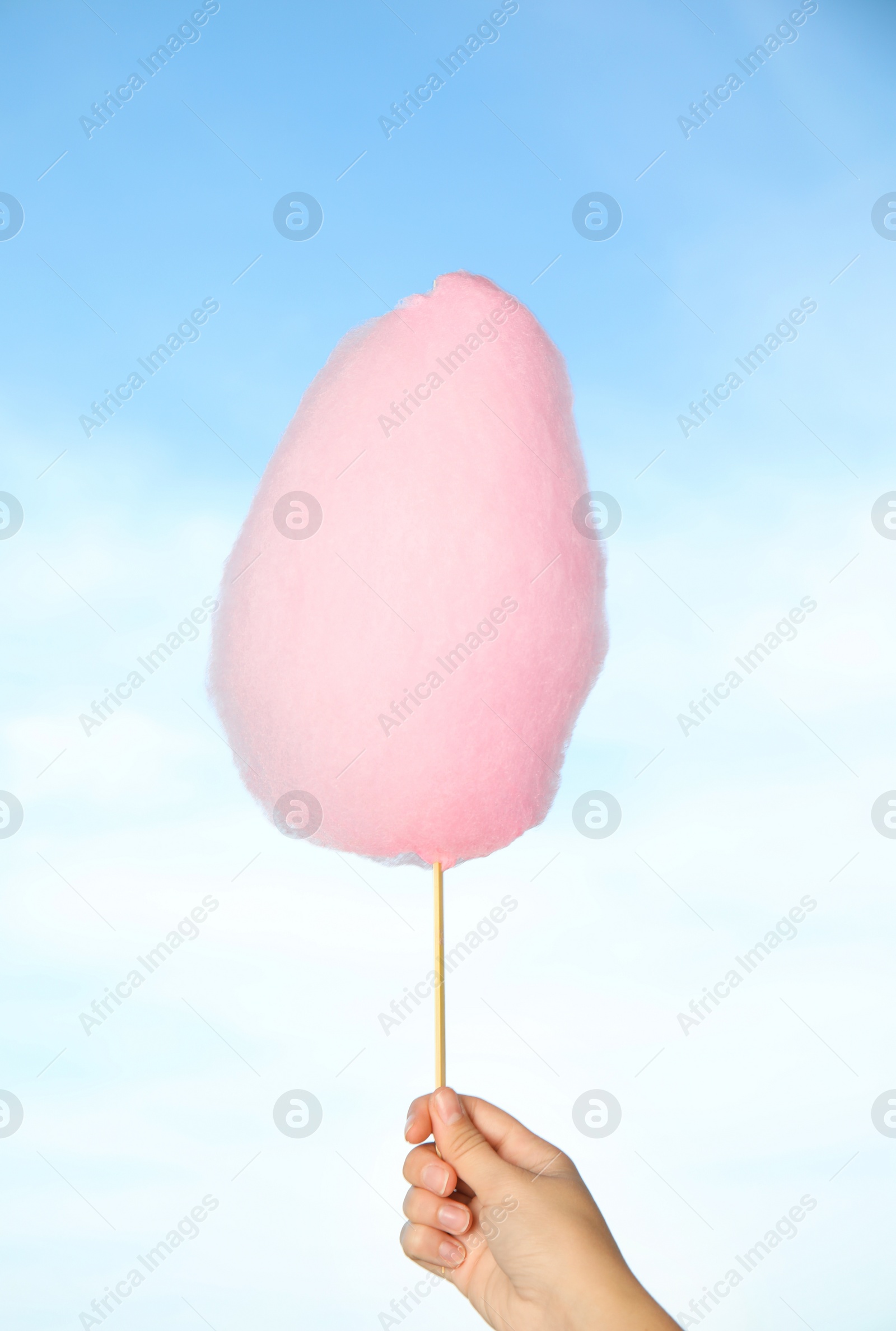 Photo of Woman holding sweet pink cotton candy on blue sky background, closeup view