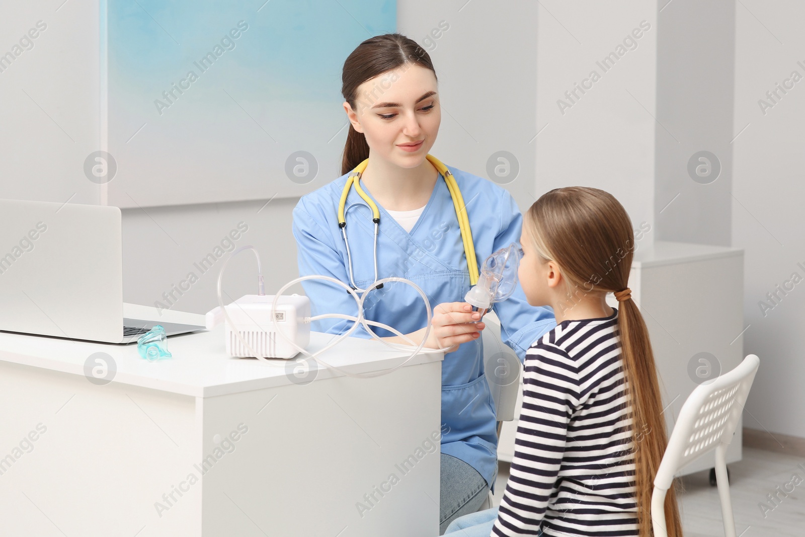 Photo of Medical assistant helping sick little girl with nebulizer inhalation in hospital