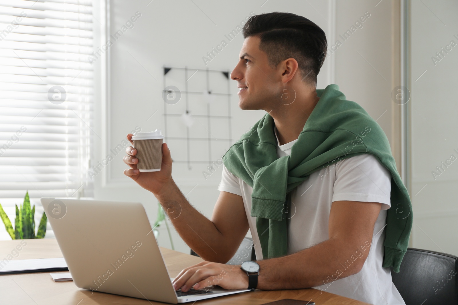 Photo of Freelancer with cup of coffee working on laptop at table indoors