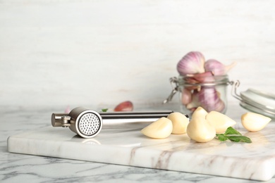 Photo of Garlic press and cloves on marble board. Kitchen utensil