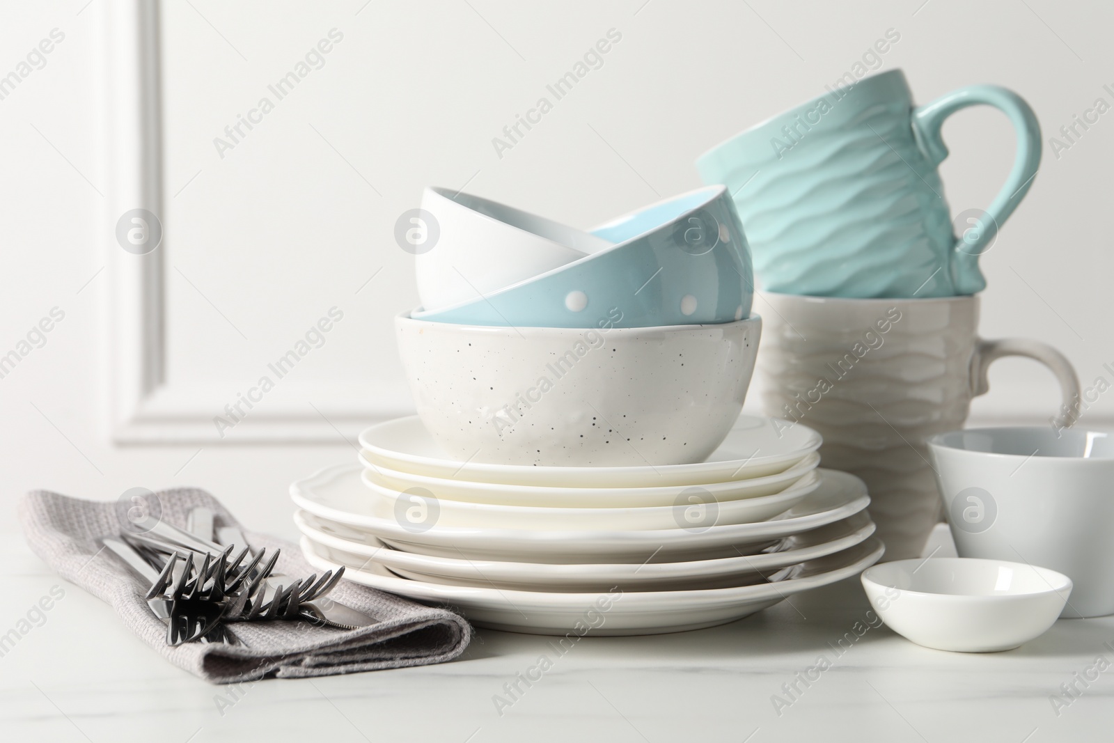 Photo of Beautiful ceramic dishware, cups and cutlery on white marble table