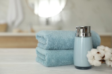 Photo of Clean towels, cotton flowers and soap dispenser on white wooden table in bathroom