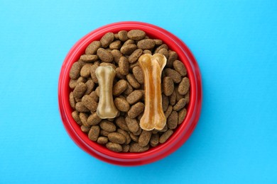 Chew bones and dry dog food on light blue background, top view