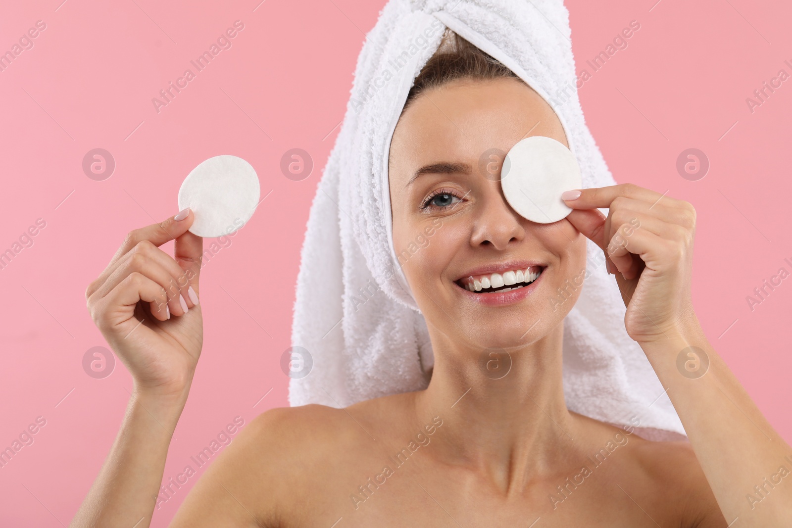 Photo of Smiling woman removing makeup with cotton pads on pink background