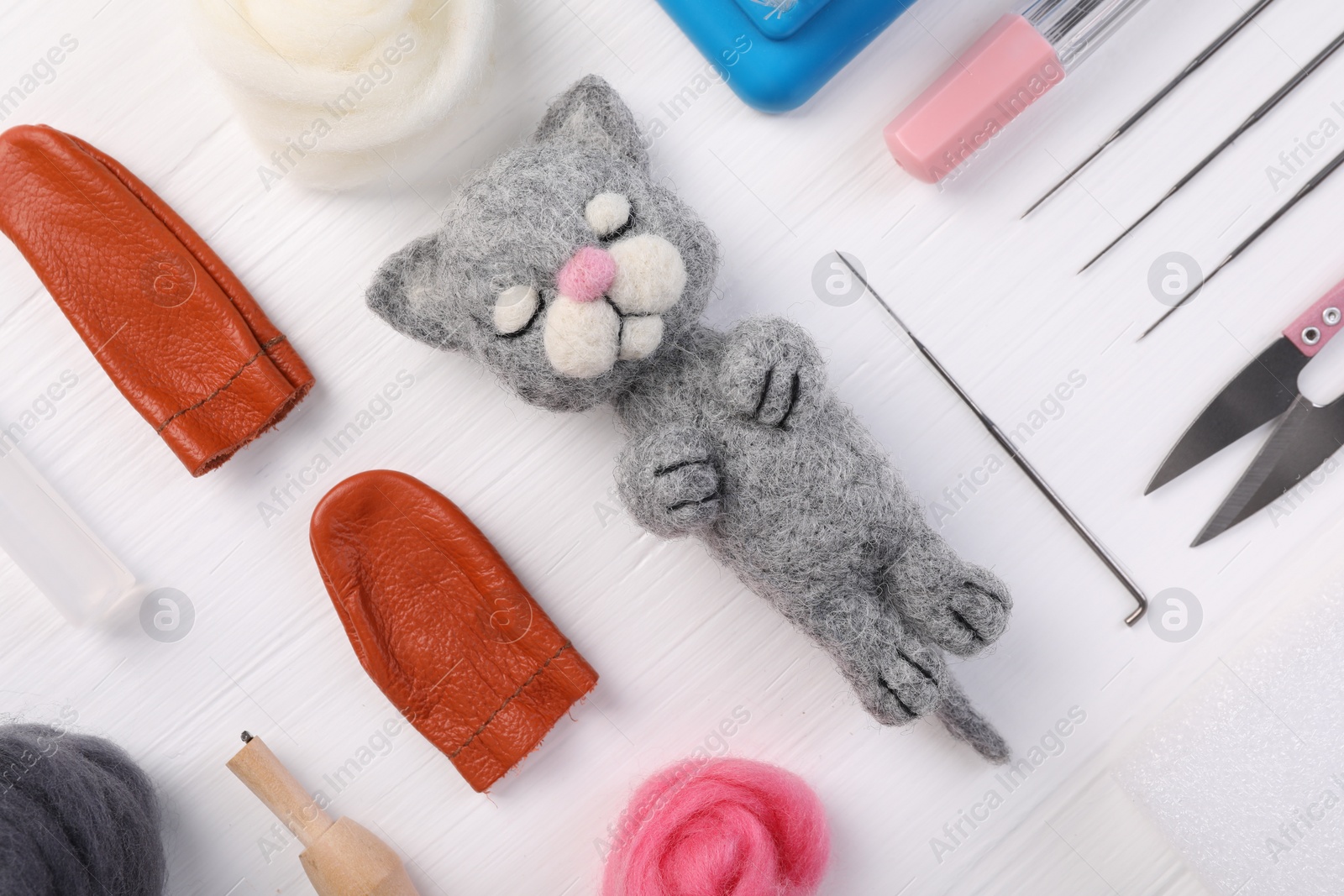 Photo of Felted cat, wool and different tools on white wooden table, flat lay