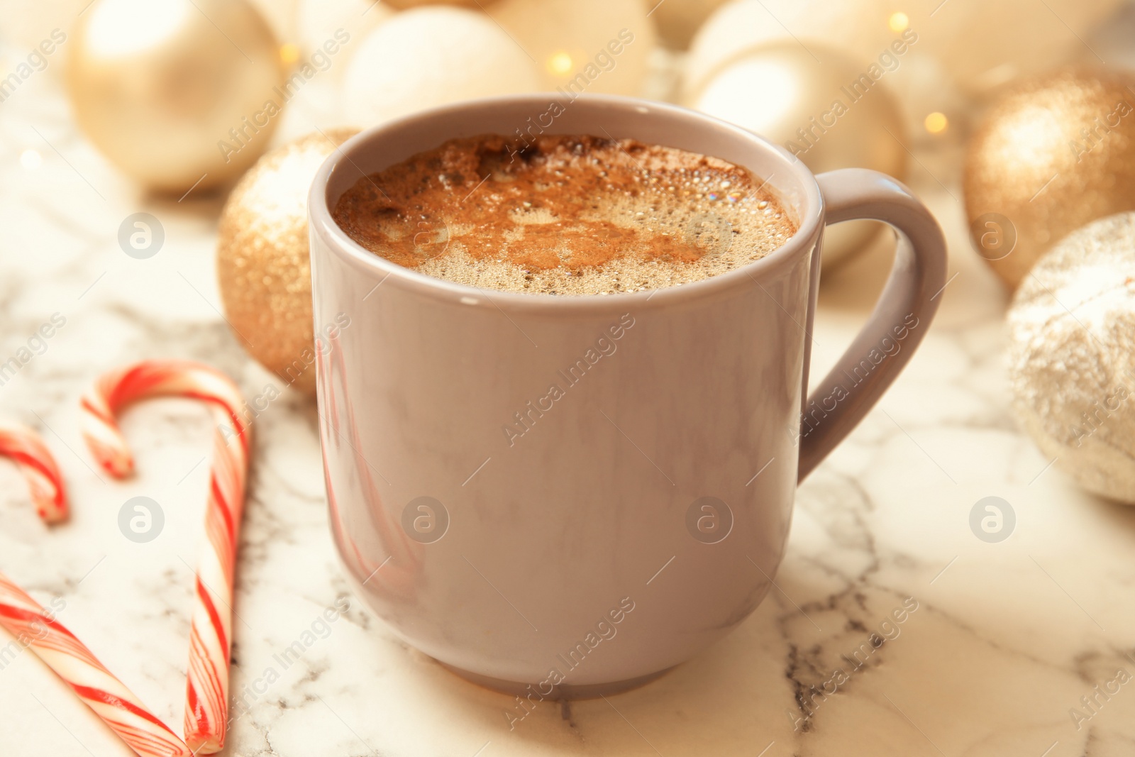 Photo of Cup of hot winter drink, candy canes and Christmas balls on marble table. Cozy season