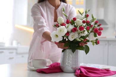 Woman with bouquet of fresh flowers in stylish vase at table, closeup