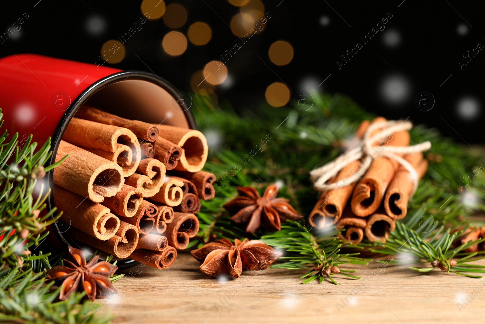 Image of Cinnamon in red mug and anise surrounded by fir tree branches on wooden table, closeup