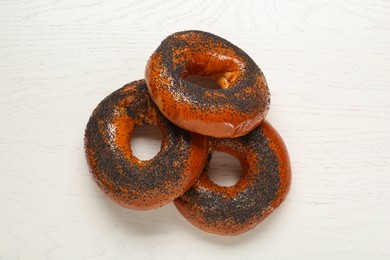 Photo of Delicious fresh bagels with poppy seeds on white wooden table, flat lay