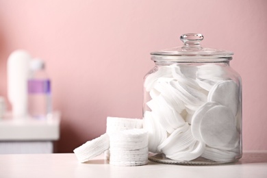 Photo of Glass jar with cotton pads on table in bathroom, space for text