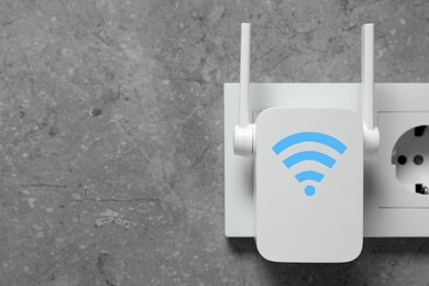 Image of New modern repeater with Wi-Fi symbol plugged into socket on concrete wall, space for text