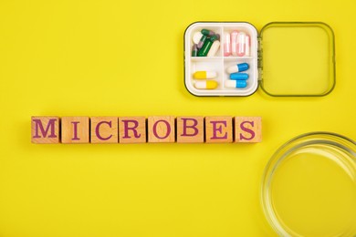 Photo of Word Microbes made with wooden cubes, pill box and magnifying glass on yellow background, top view
