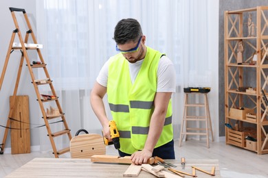 Young worker using electric drill at table in workshop