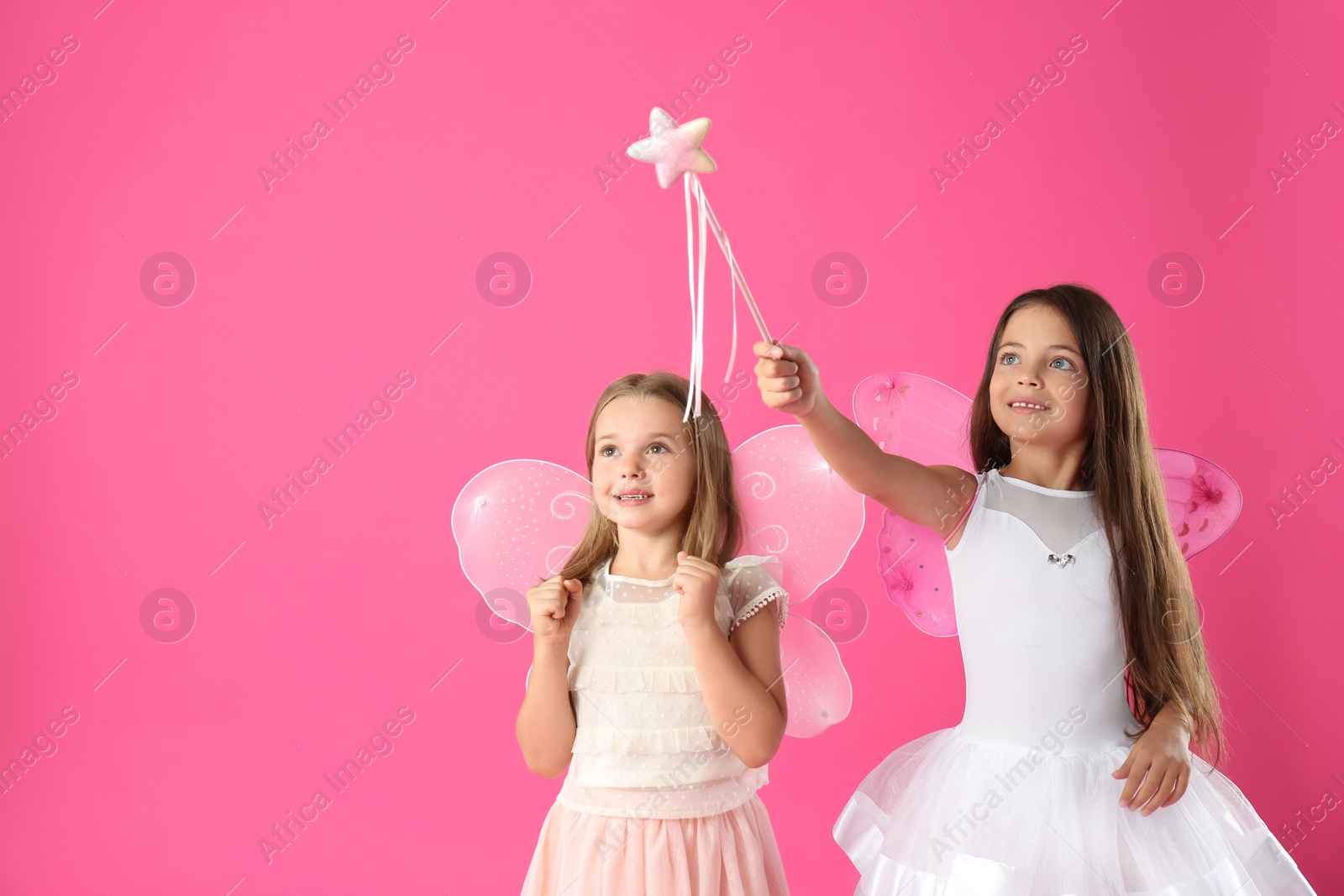 Photo of Cute little girls in fairy costumes with wings and magic wand on pink background. Space for text
