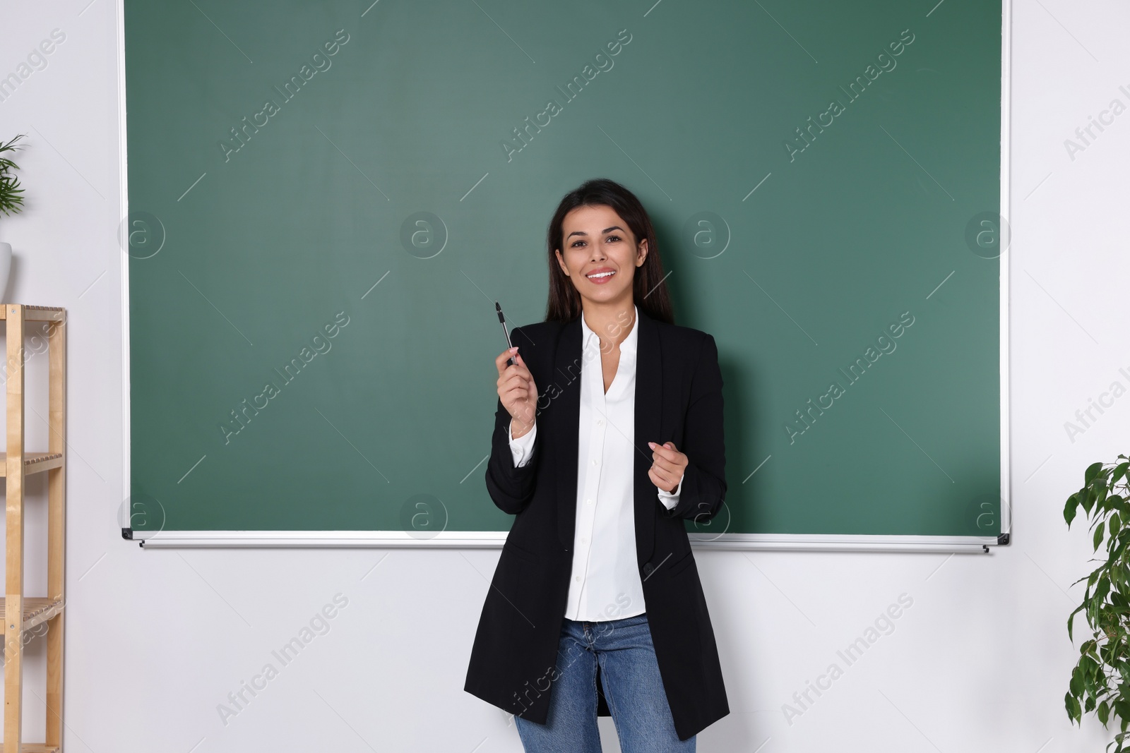 Photo of Happy young teacher giving lesson at blackboard in classroom. Space for text