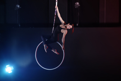 Photo of Young woman performing acrobatic element on aerial ring indoors