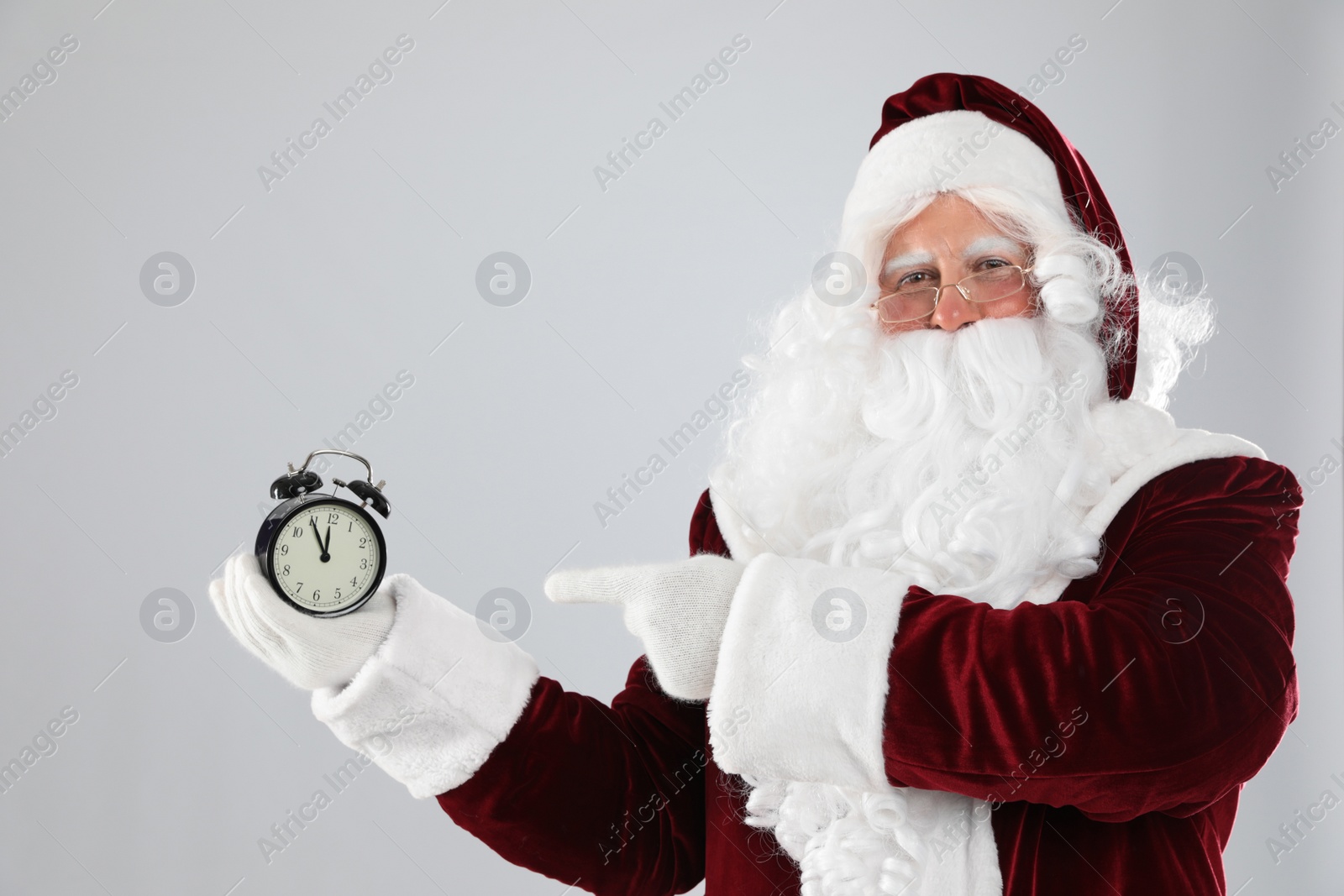 Photo of Santa Claus holding alarm clock on light grey background. Christmas countdown