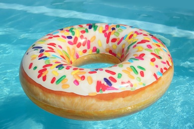 Bright inflatable doughnut ring floating in swimming pool on sunny day