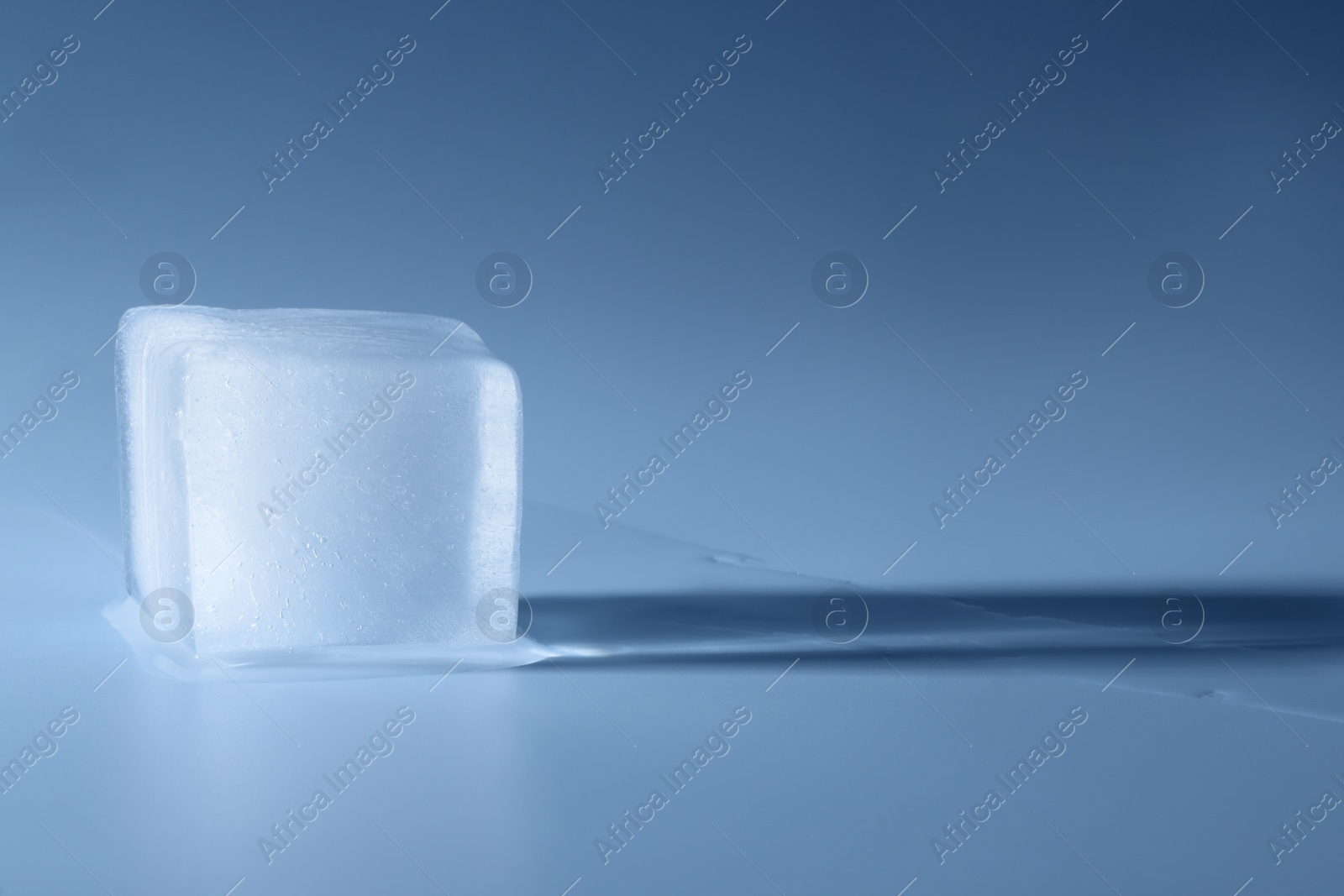 Photo of Crystal clear ice cube on light blue background, space for text