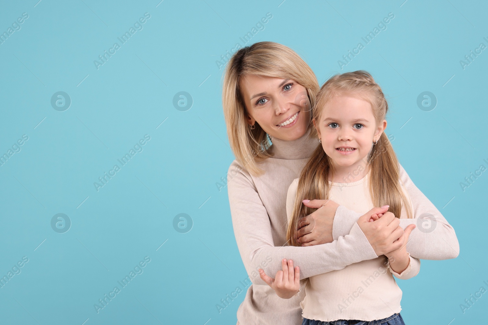 Photo of Mother hugging her happy daughter on light blue background. Space for text