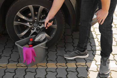 Man taking brush from bucket with car cleaning products outdoors, closeup