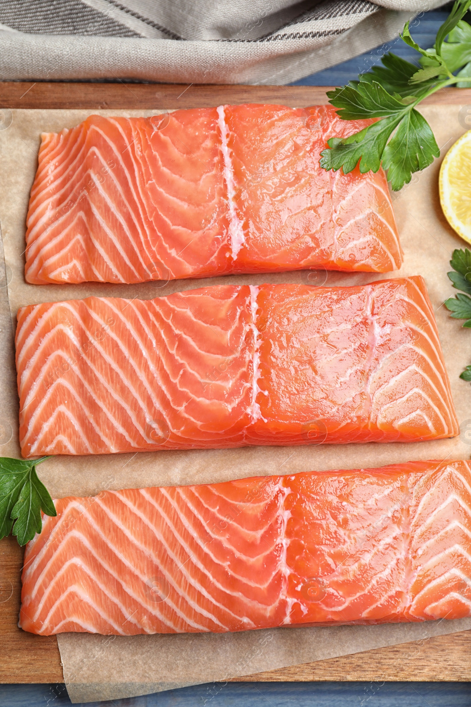 Photo of Fresh raw salmon with parsley on wooden board, flat lay. Fish delicacy