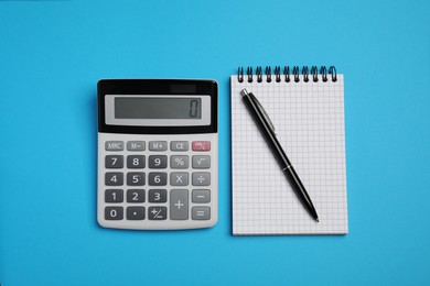 Calculator, notebook and pen on light blue background, flat lay