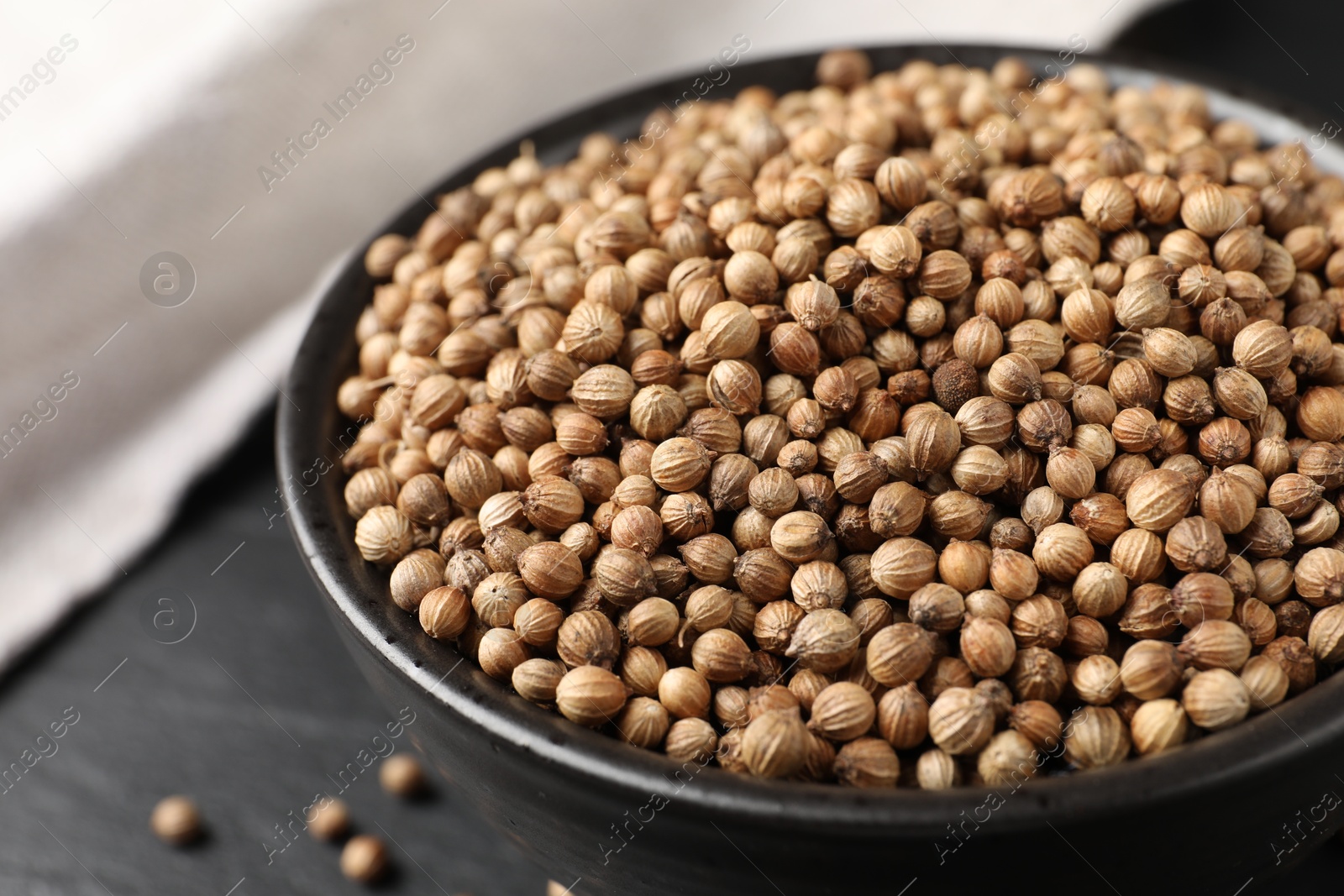 Photo of Dried coriander seeds in bowl on dark gray table, closeup