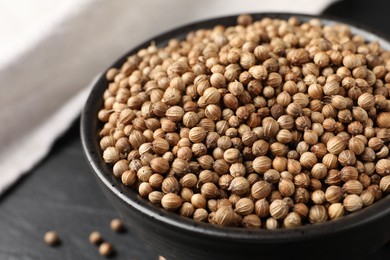 Dried coriander seeds in bowl on dark gray table, closeup