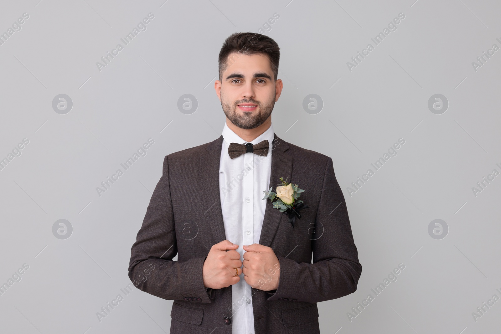 Photo of Handsome young groom with boutonniere on light grey background. Wedding accessory