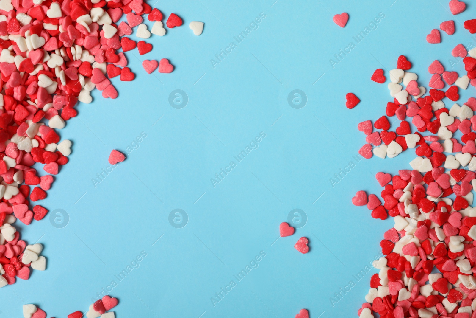 Photo of Bright heart shaped sprinkles on light blue background, flat lay. Space for text