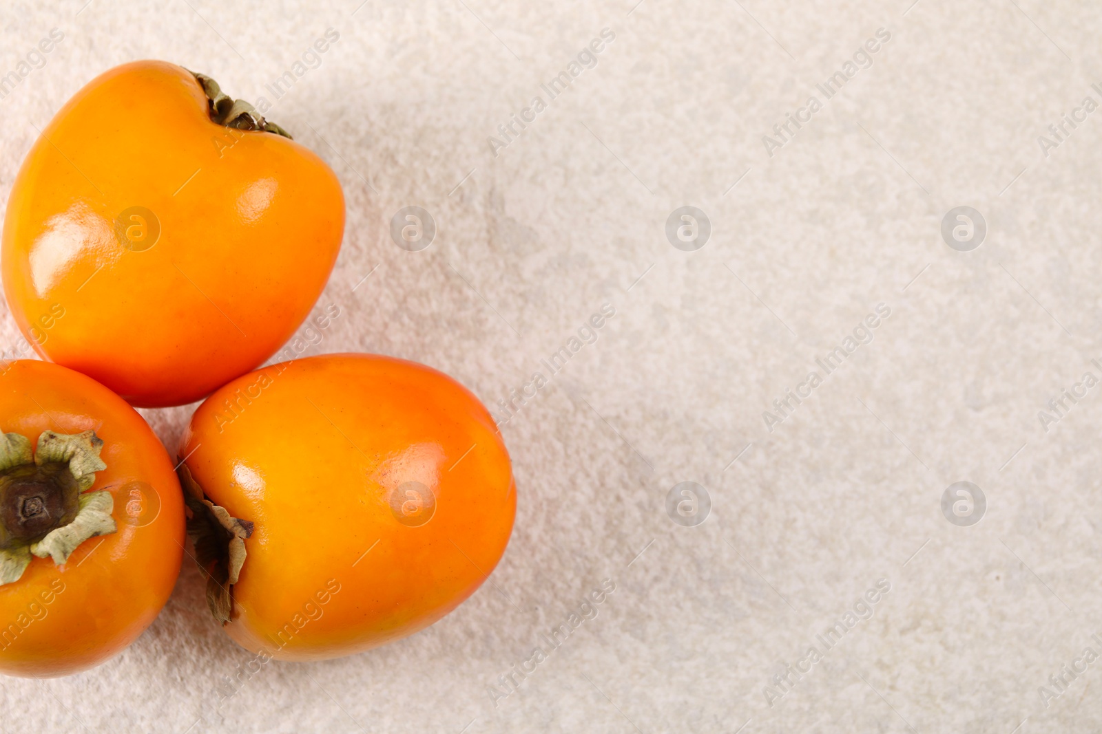 Photo of Delicious ripe persimmons on light textured table, top view. Space for text