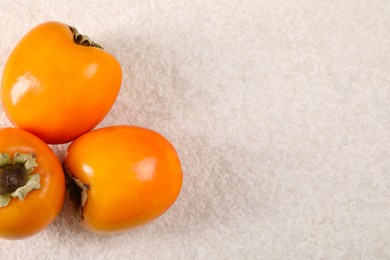 Photo of Delicious ripe persimmons on light textured table, top view. Space for text