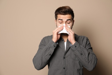 Photo of Handsome young man blowing nose against color background. Space for text