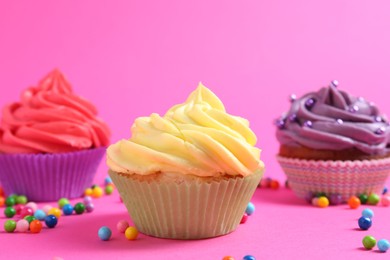 Photo of Delicious cupcakes with bright cream and sprinkles on pink background, closeup