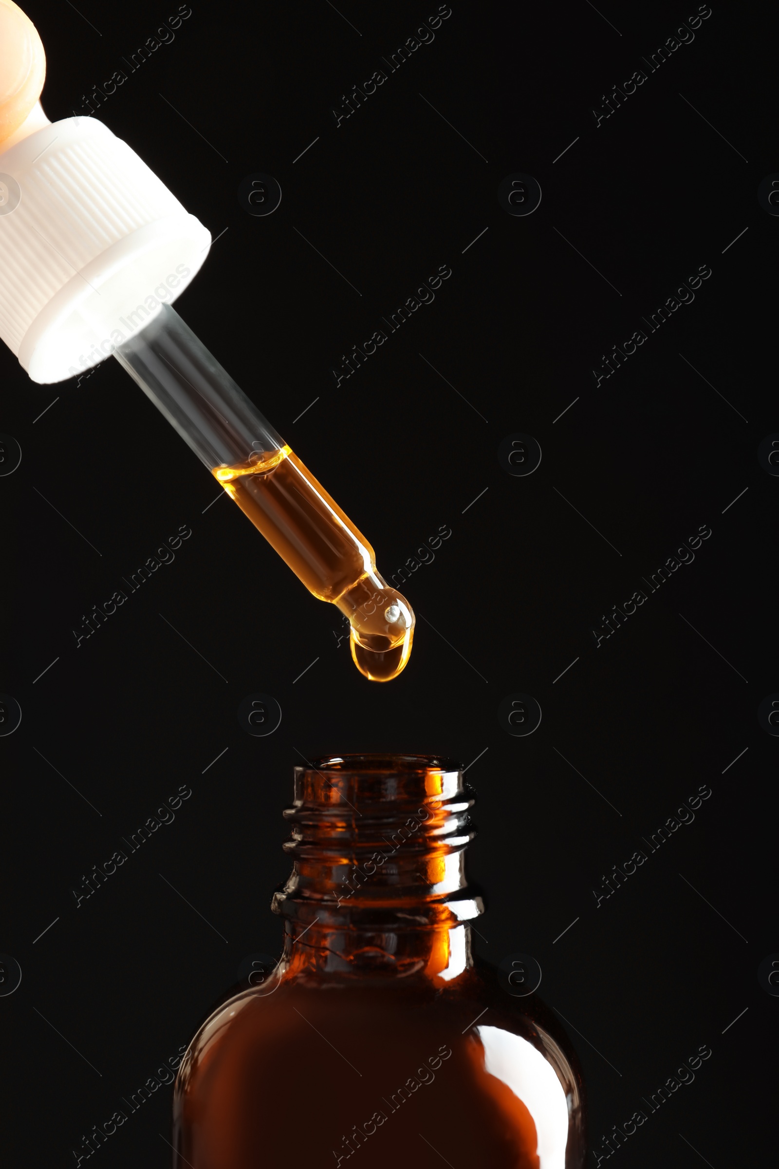 Photo of Pipette with oil over bottle on black background