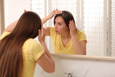 Photo of Young woman with hair loss problem looking in mirror indoors