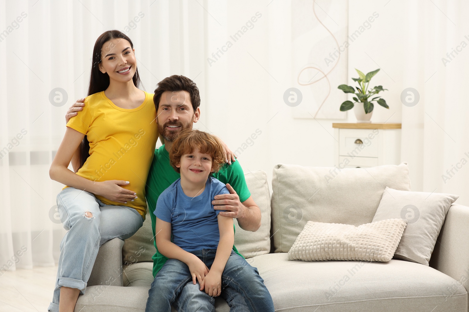 Photo of Family portrait of pregnant mother, father and son in house. Space for text