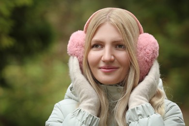 Photo of Young beautiful woman wearing warm earmuffs outdoors